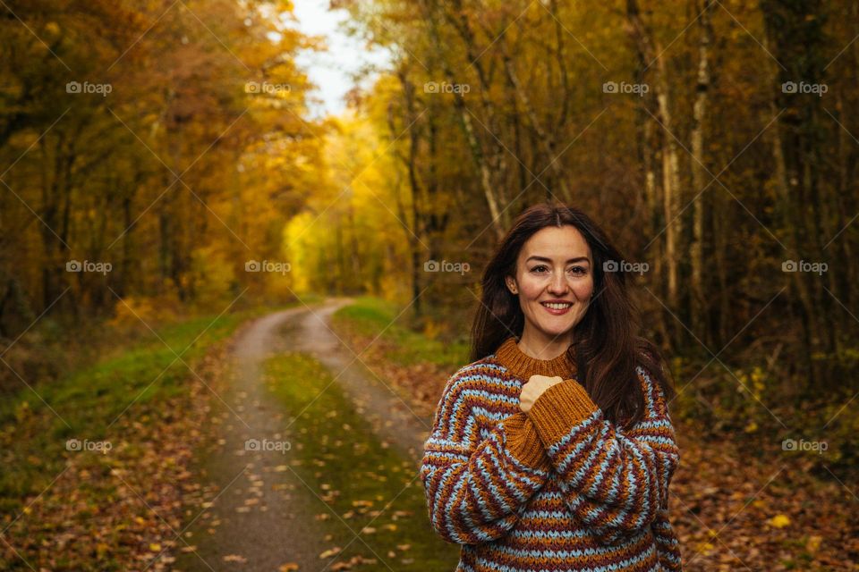 Happy smiling woman, in a wonderful forest, dressed in autumn colors on a beautiful sunny day.