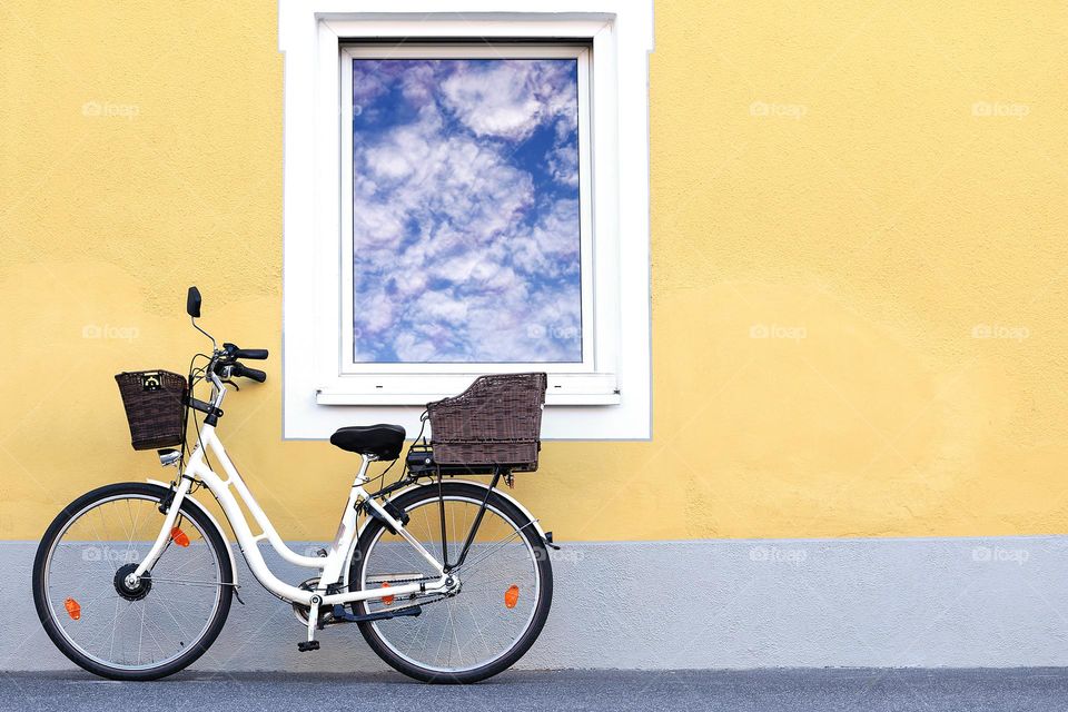 A lady's bicycle at a yellow house with a window. Reflection of the sky in the window