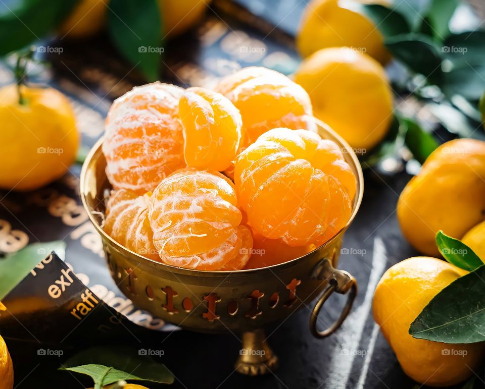 Close up of peeled mandarins in a brass fruit bowl on blurred background.