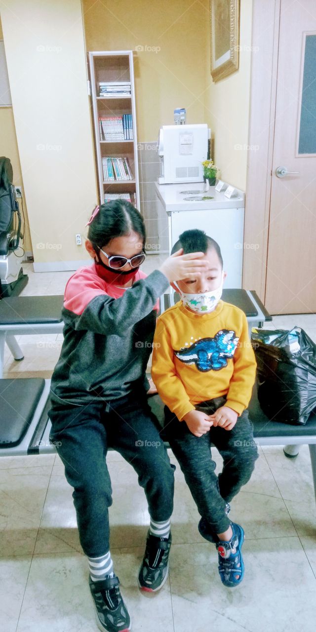 the big sister holding his younger brothers forehead to check his condition if his good or not.