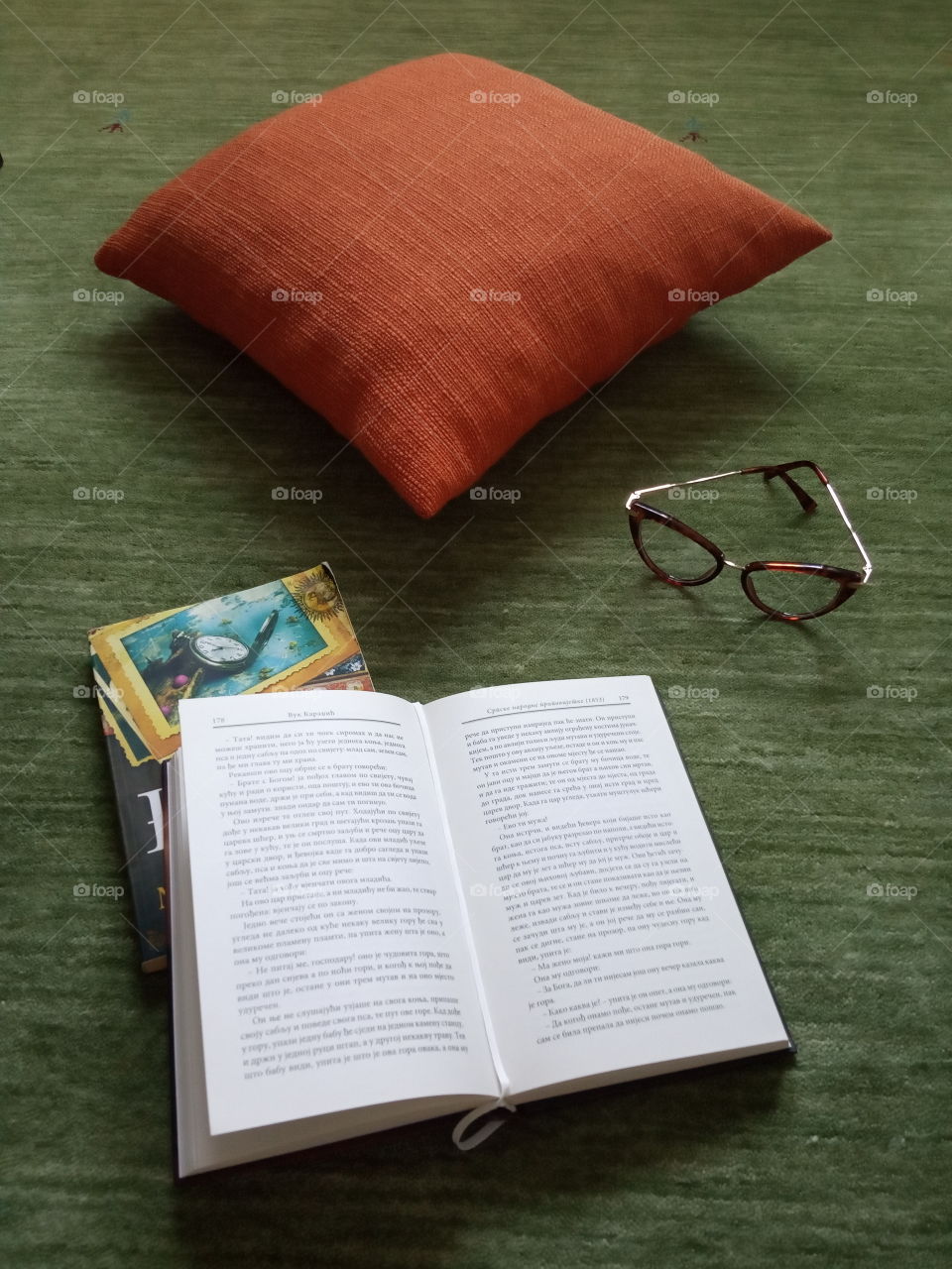 Interesting aregment of light and shadows, green and orange colour, and cloth texture, features pillow books and glasses.