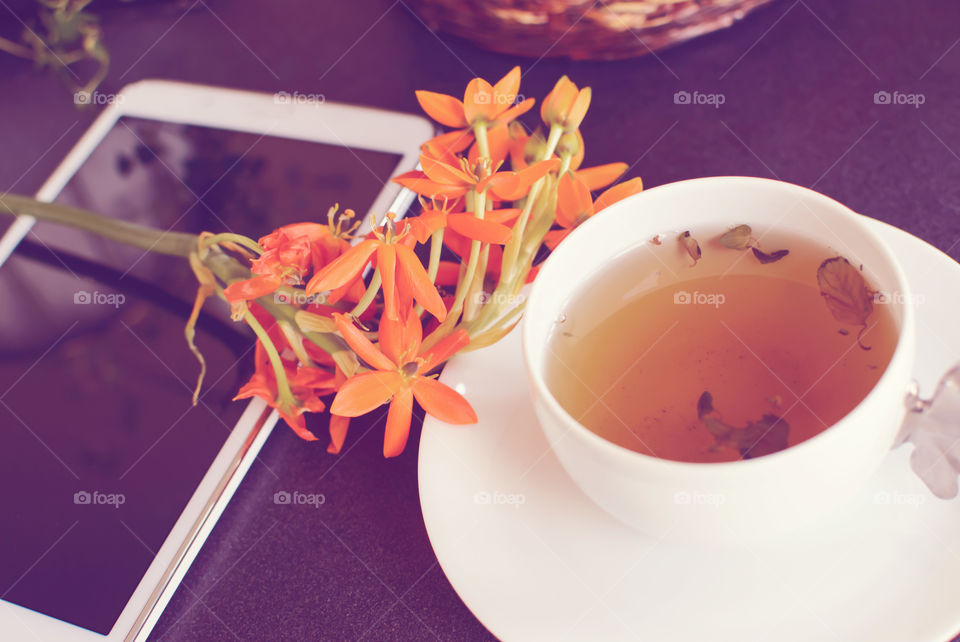 Mobile tablet next to Cup of organic natural tea with fresh flowers conceptual tranquility and healthy lifestyle background home or business environment image