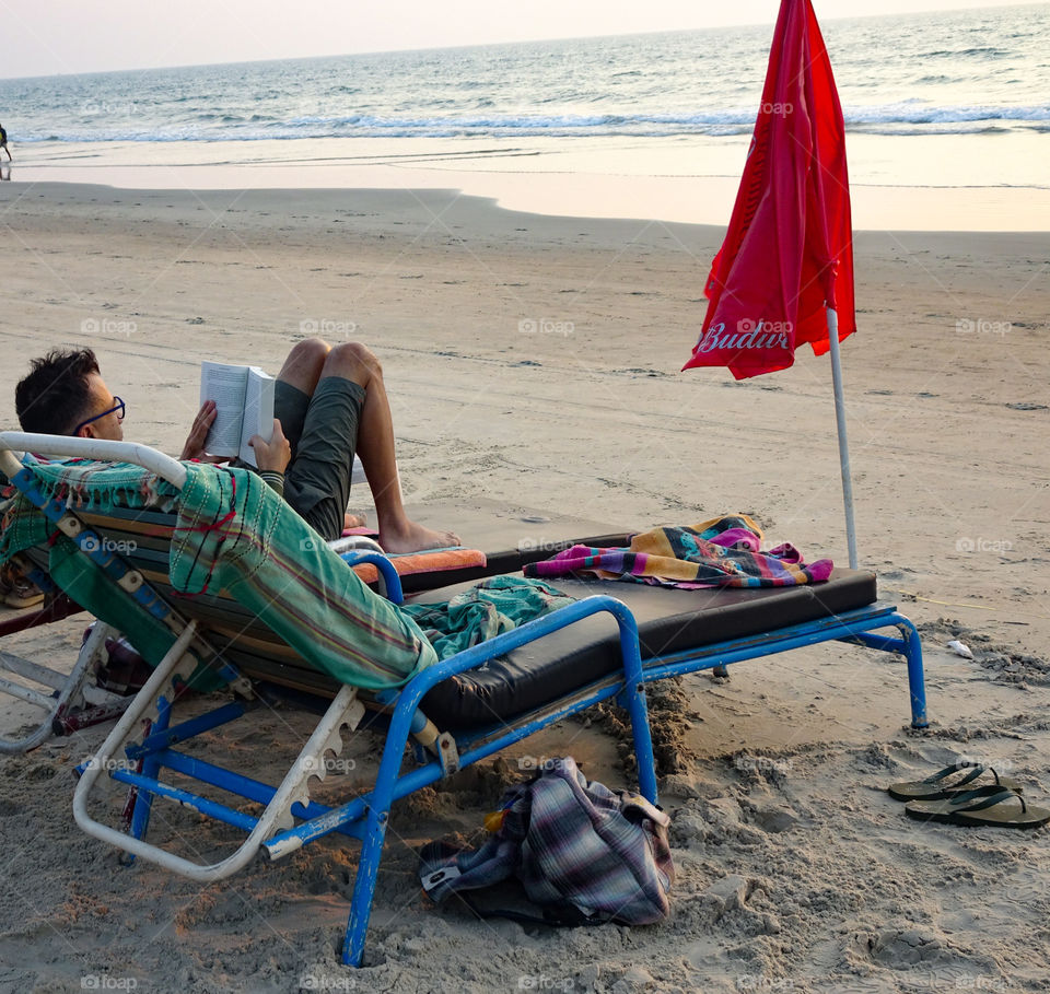 man reading a book lying sitting on a chair on the beach in summer