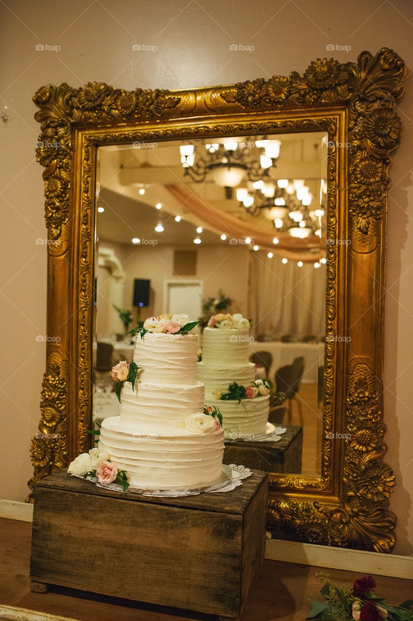 White wedding cake with pastel flowers against antique mirror 