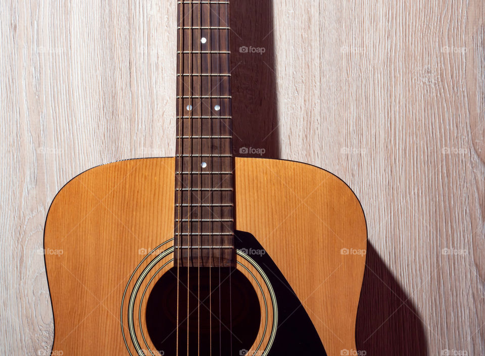 A brown classic acoustic guitar lies on a light wooden background.