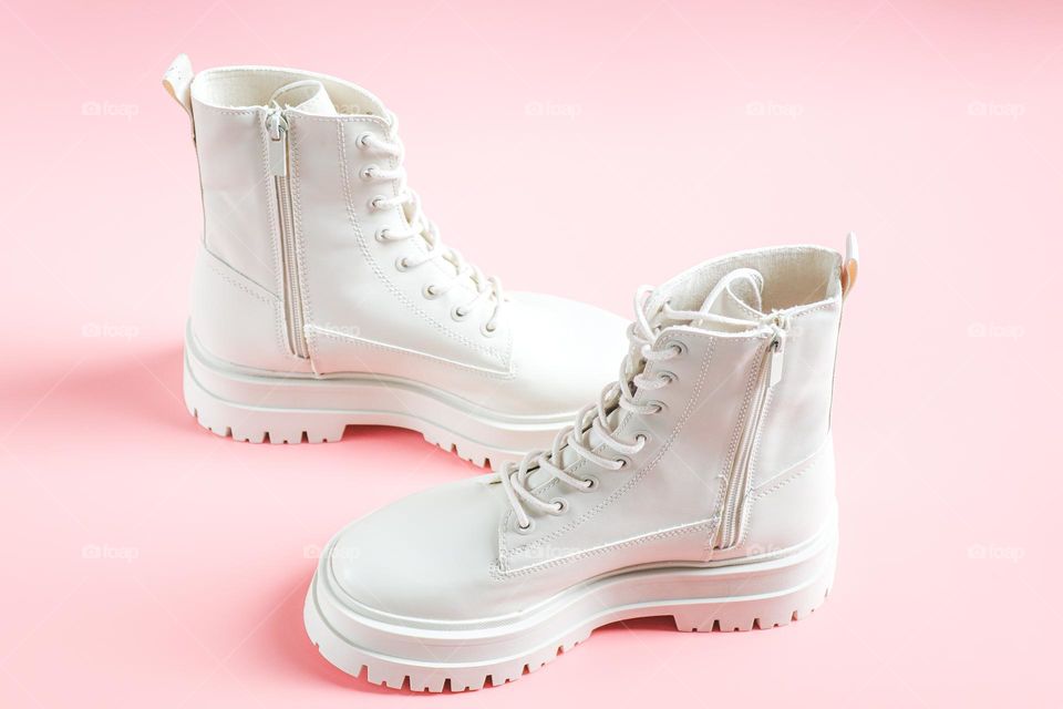 One pair of beautiful white Martens brand shoes on a rough tractor sole with lacing stand in the center on a light pink background,flats Lay. The concept of fashionable women's shoes.