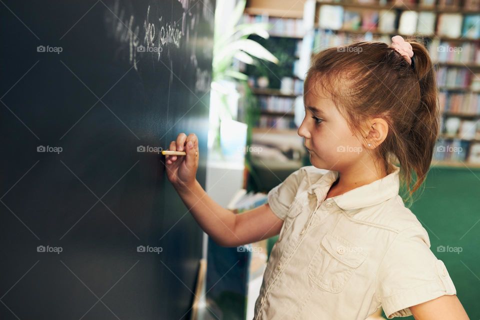 Little girl writing on blackboard. Smart student put solve on chalkboard. Back to school. Child having class. Schoolgirl learning at primary school. Elementary education