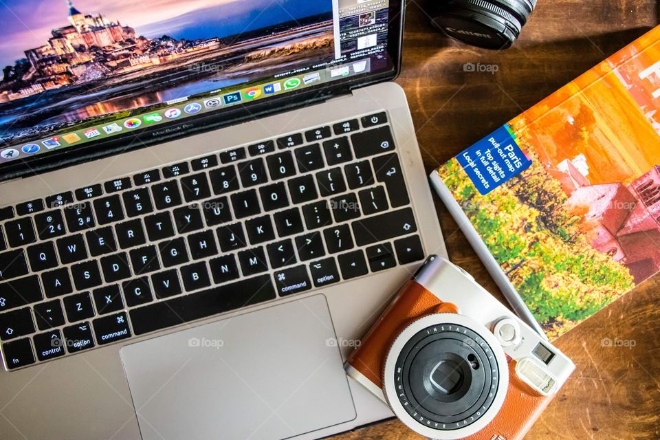 Flatlay photograph of a desk with a laptop, travel book and an instax camera.