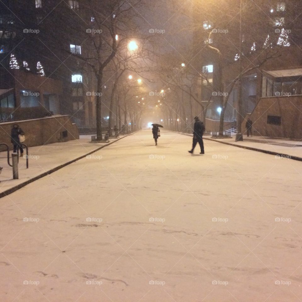 New Yorkers wandering down a snowy winter street at night. 