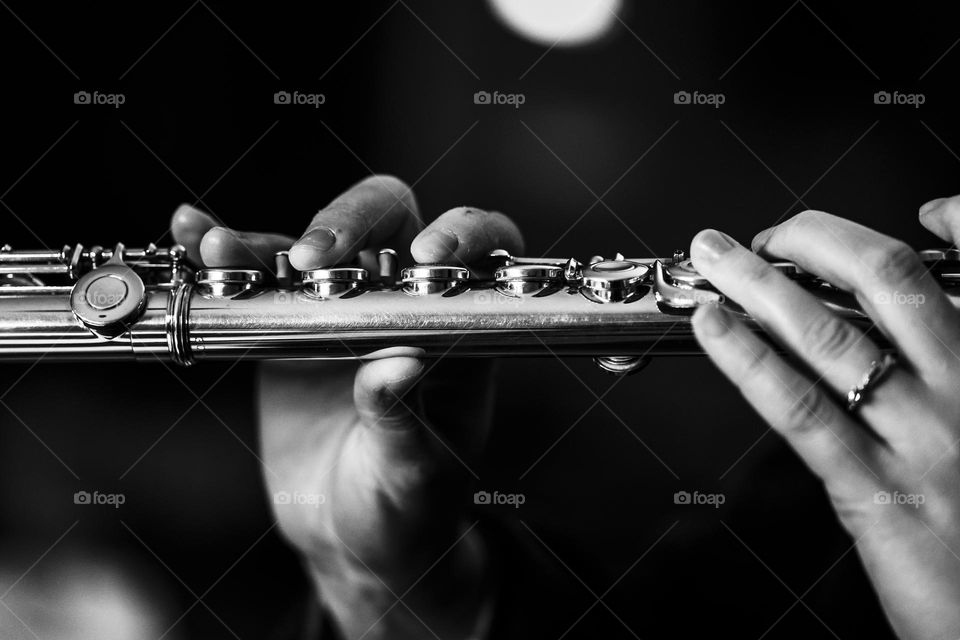A black and white portrait of a flutist playing the silver flute. the fingers of the musician are pressing on the valves to hit a note.