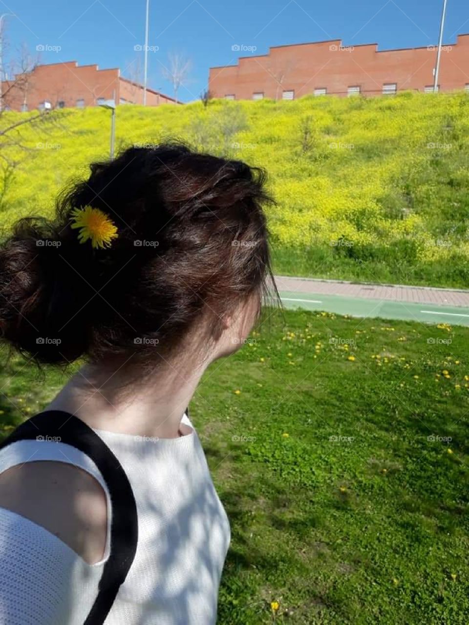 Woman near a hill covered with dandelions. Yellow flowers with green grass and orange brick structures.