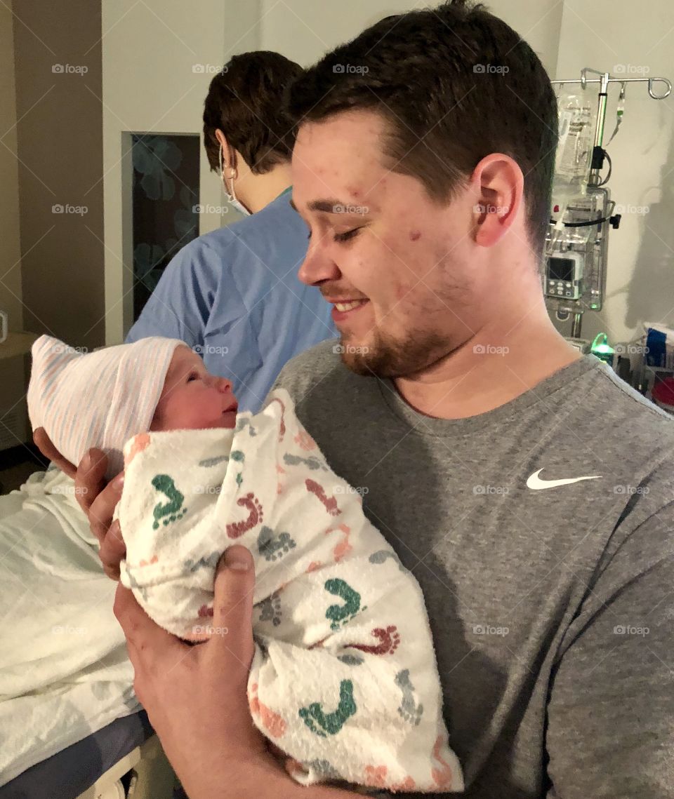 New father holding and smiling at firstborn son in hospital room