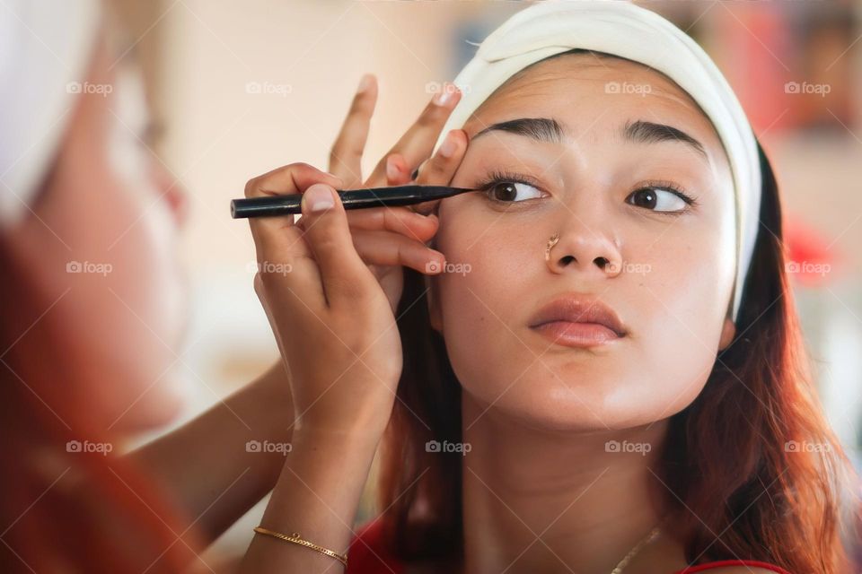 Young woman is using an eye liner in front of a mirror