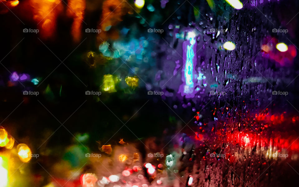 A wet glass window after hit by a rain at night, showing colorful light from outside