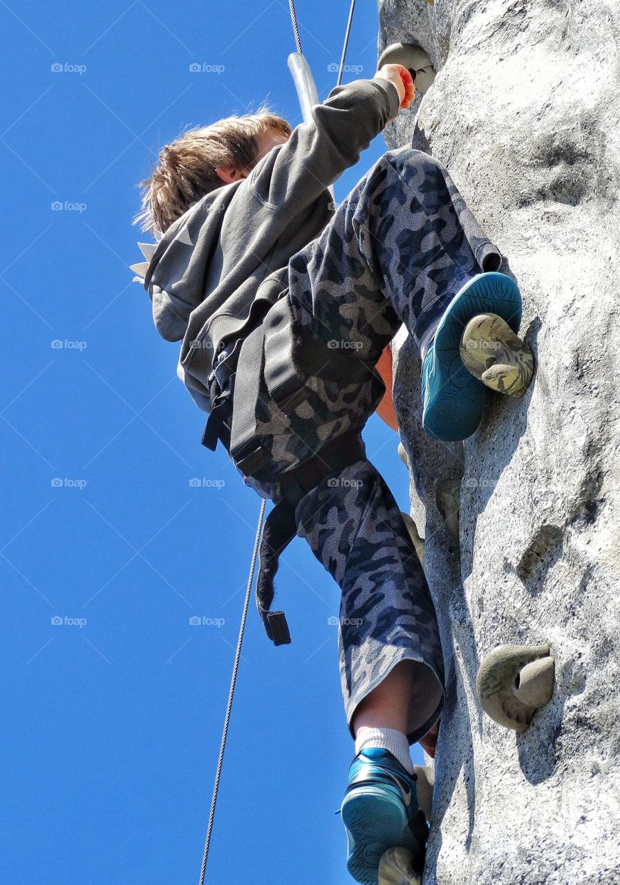 Vertical Climb. Boy Scaling A Rock Wall
