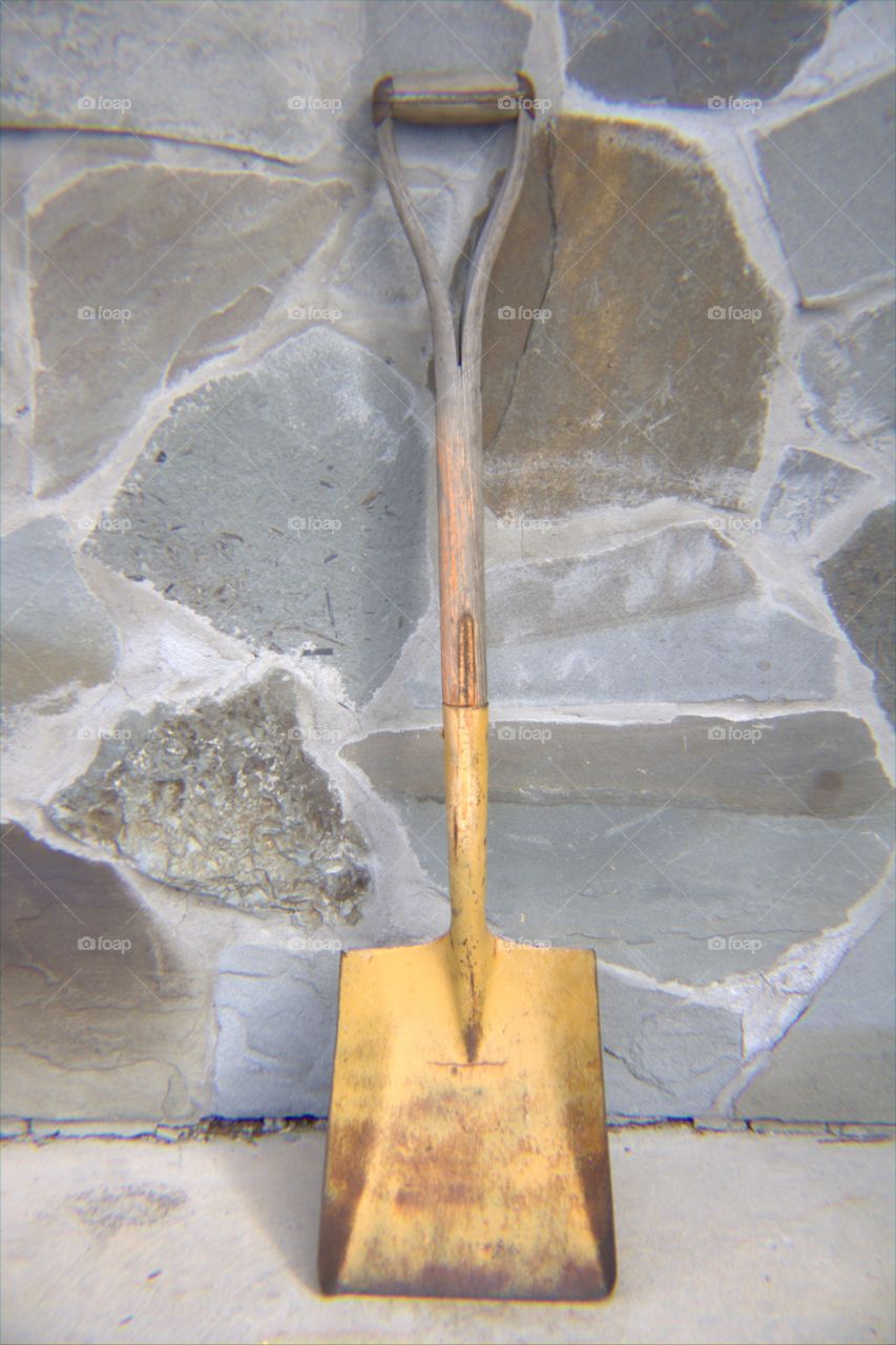 Yellow Shovel Leaning Against a Stone Wall