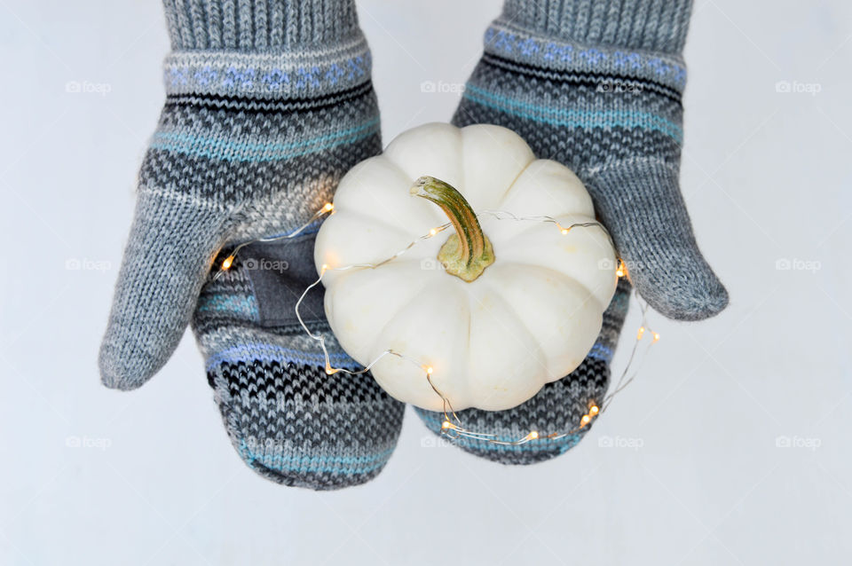 Close-up top view of a person's gloved hands holding a white pumpkin with a string of lights