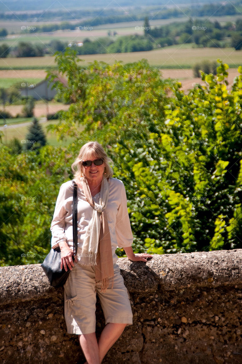 Woman wearing sunglasses means on the stone wall in front of wine