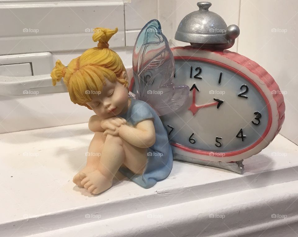 A pretty fairy sleeping in front of a clock.