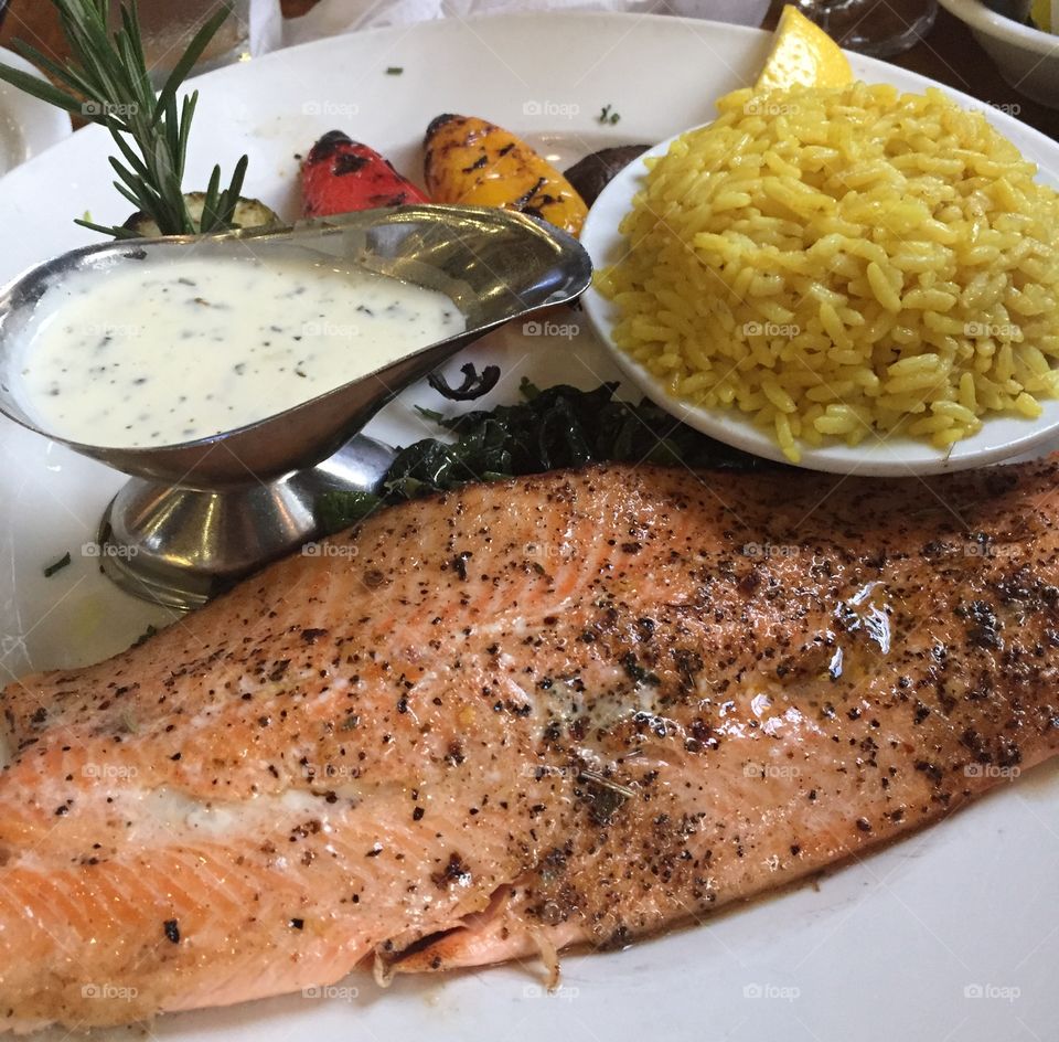 Salmon with sauce and spices with a bowl of rice and vegetables on the side
