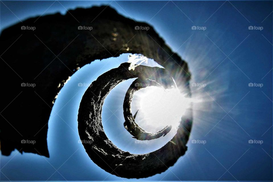 rusty metal spiral shaped object found at an abandoned building site held up in the blue sky with the sunlight falling trough the end