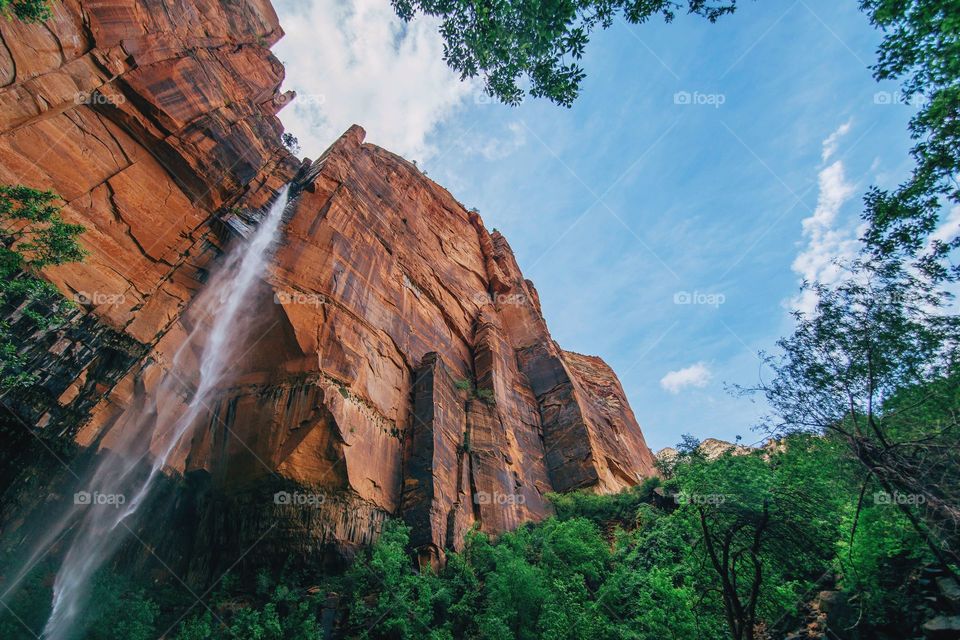 A magnificent low-angle shot of a red rock face with a cascading waterfall
