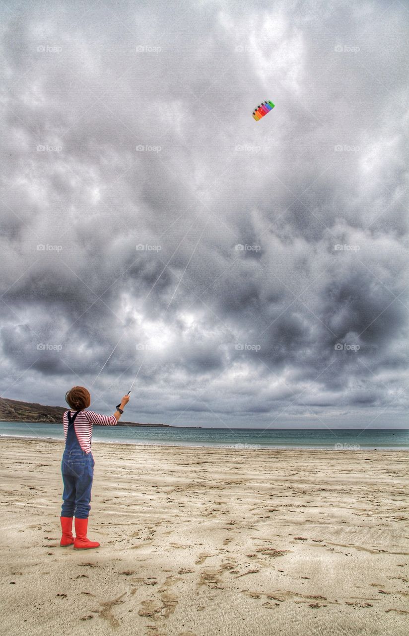 Girl Flying a Colourful Kite. A girl on red wellies flying a colourful kite on a deserted sandy beach.