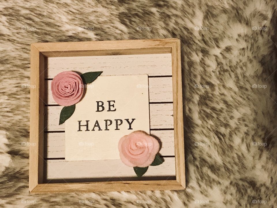 New Years resolutions to be a Happy person !! A wooden sign with beautiful pink roses saying Be Happy written on it displayed on a fuzzy rug. USA, America