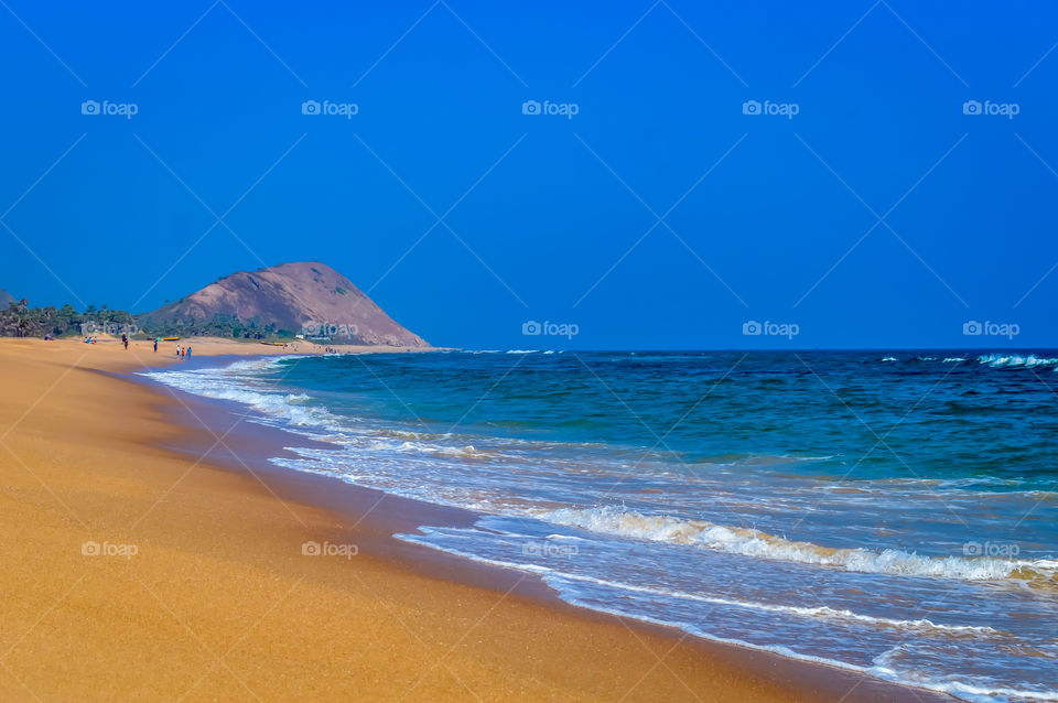 Wild Empty Tropical beach, vibrant yellow sand, bright blue sky, crystal clear waters with water crashing on the shore at daytime on a sunny day in in as landscape style may be used as a background, wallpaper, screen saver Travel vacation concept. Th