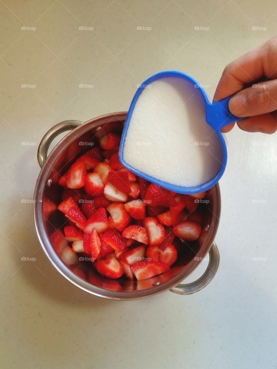 Hand pouring sugar over pot of strawberries