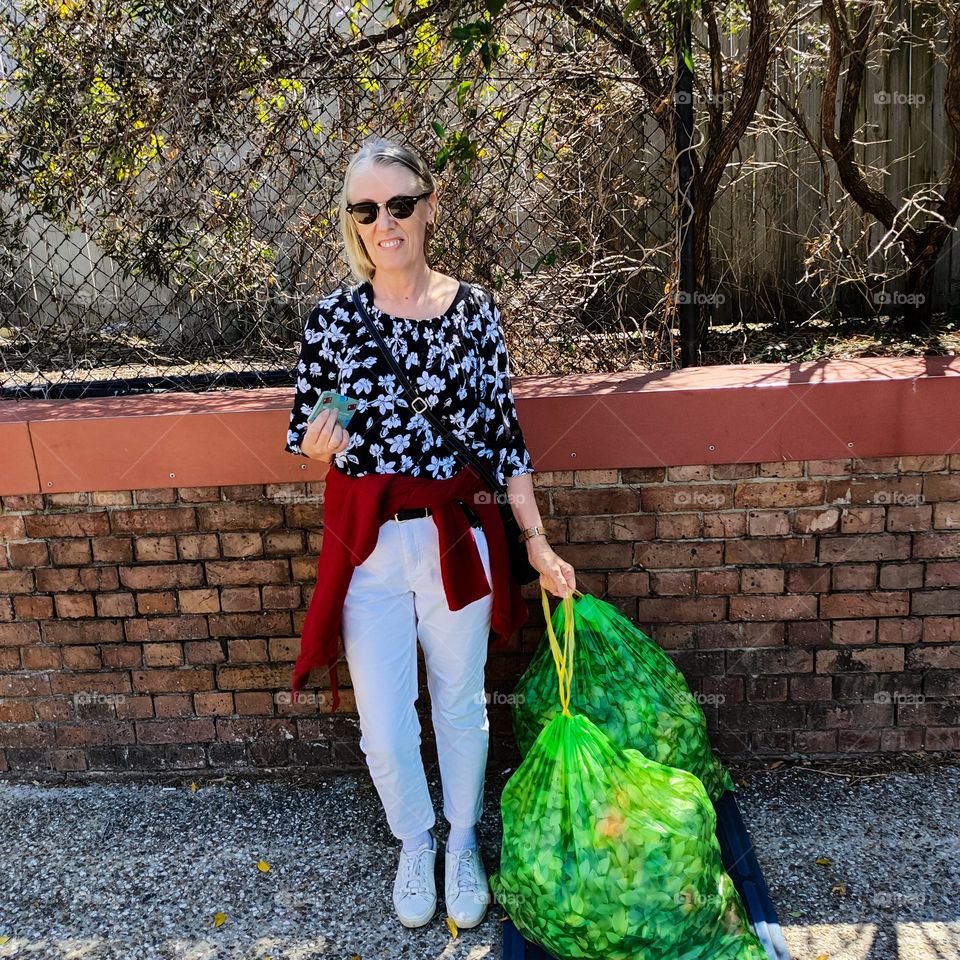 Blonde scandinavian woman taking two bags of bottles and cans to a recycling centre