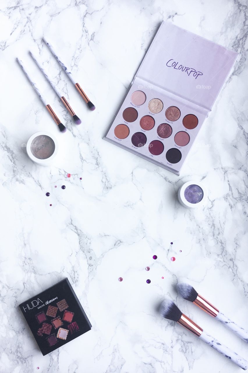 Makeup flat lay on a marble background, light pink, eyeshadow palettes and makeup brushes.