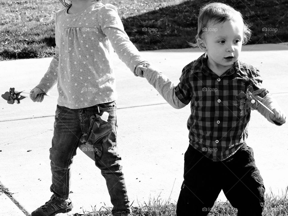 A toddler boy desperately drags his big sister to the grass to play on a sunny spring day. 