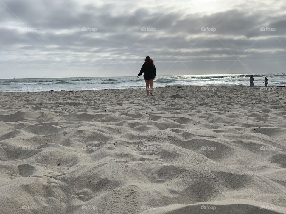 Girl walking along the sand alone towards the beach coast and the waves on a cloudy overcast day