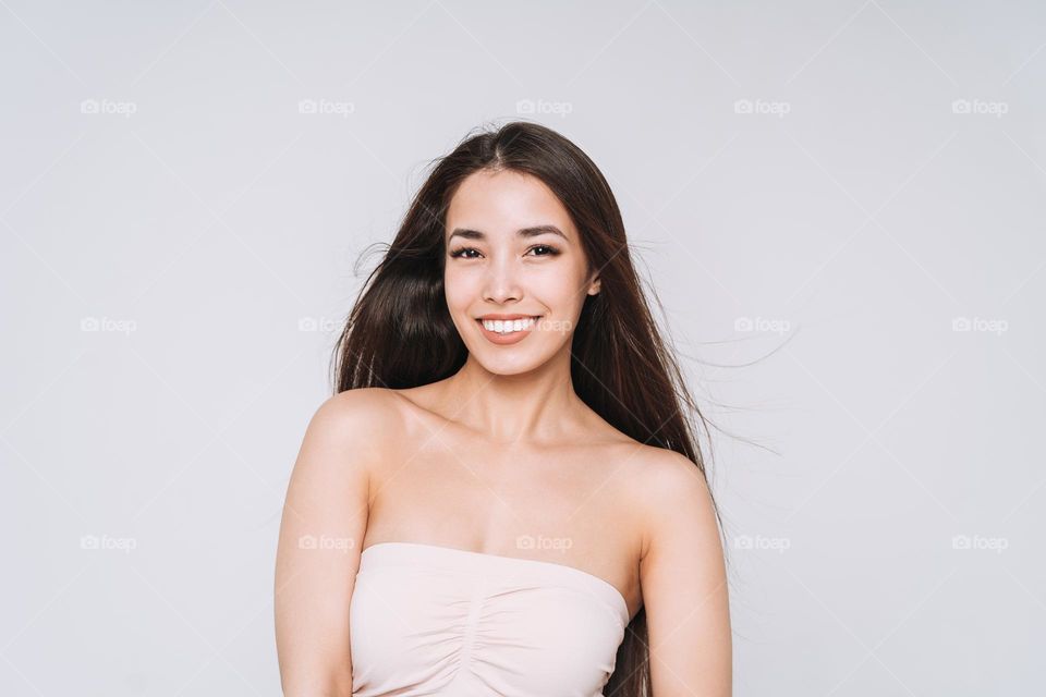 Beauty portrait of happy young beautiful asian woman with healthy dark long hair in top bando on white background isolated