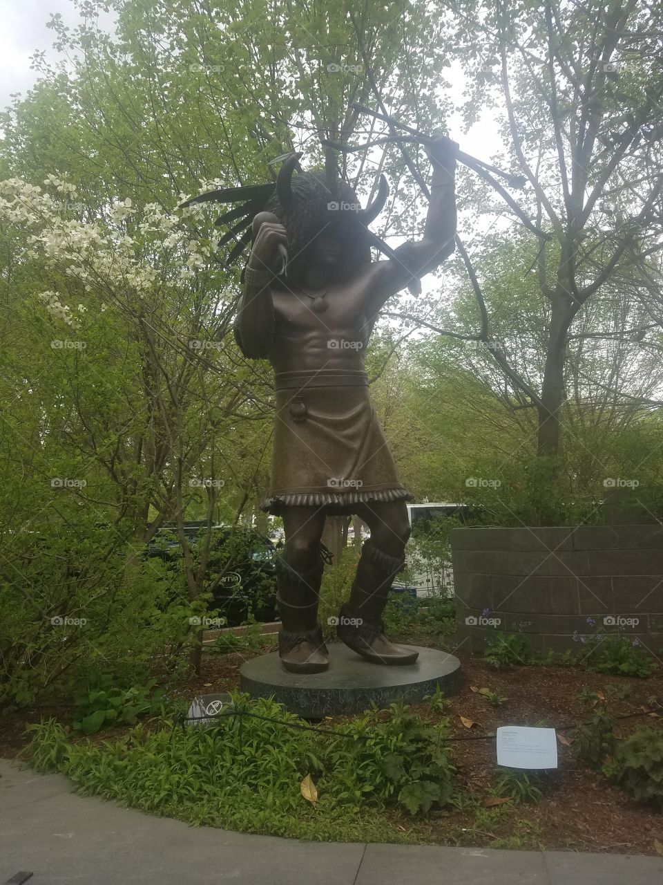 A Native American statue depicting him in a warrior stance. The statue is surrounded by forestry.