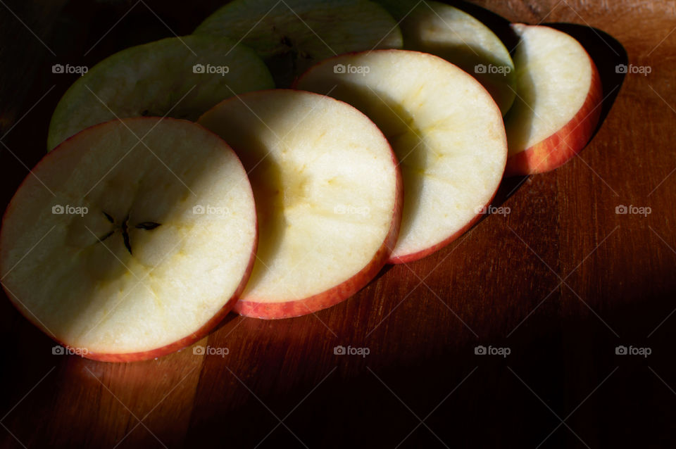 Beautiful crisp sliced red apple cross section in row cut in circle shape with seeds on dark wood healthy lifestyle eating choices food photography 