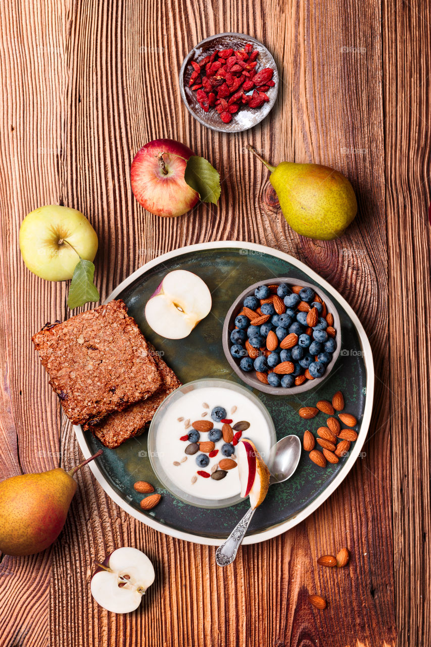 Breakfast on table. Yogurt with added blueberries and roasted almonds. Muesli cookie, apples and pears on wooden table. Light and healthy meal. Good quality balanced diet. Flat top-down composition