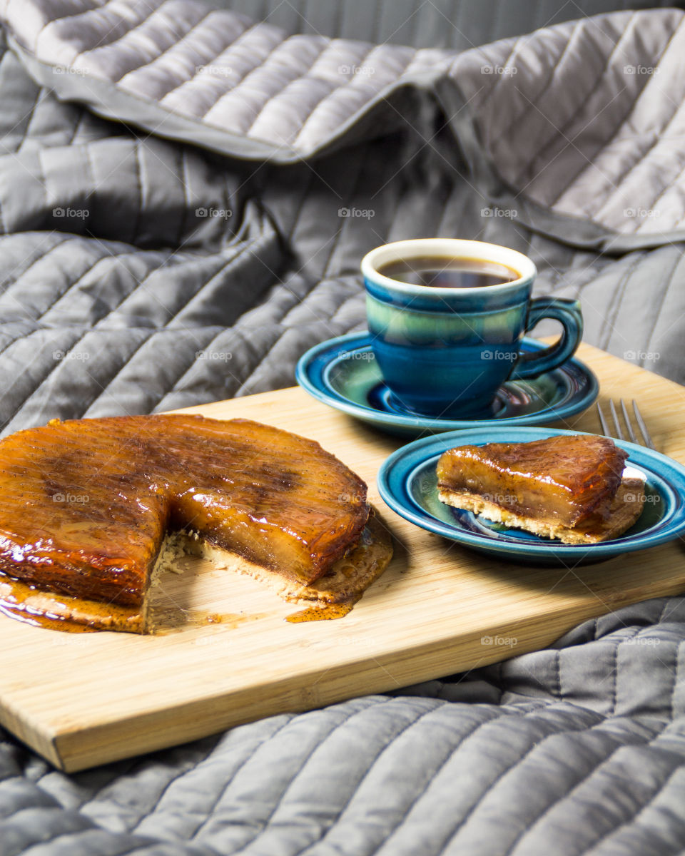 Early morning breakfast in the bed. On the tray lies a delicious french pie Tarte Tatin made of caramelized apples with cinnamon on base layer of short-dough and a steaming cup of black coffee.