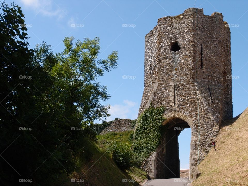 A large stone tower at Dover Castle with an arched entryway and a hole for archers to fire arrows with a walkway leading tourists to it on a warm and sunny summer day in England.