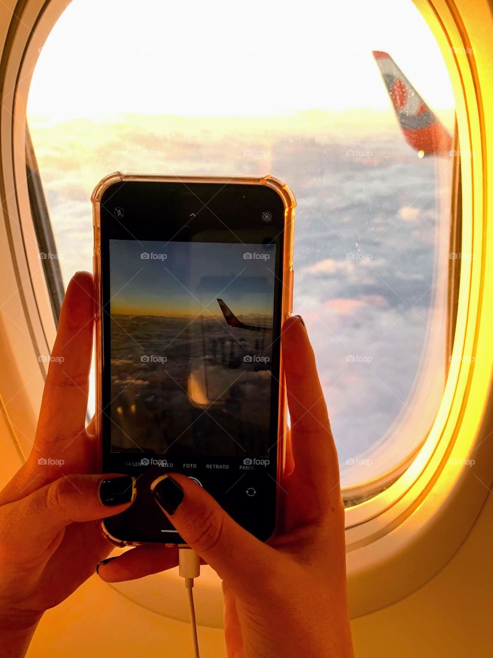 Two hands photographing the sunset through the airplane window