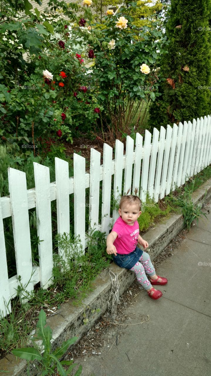 Cute little girl sitting against white fence