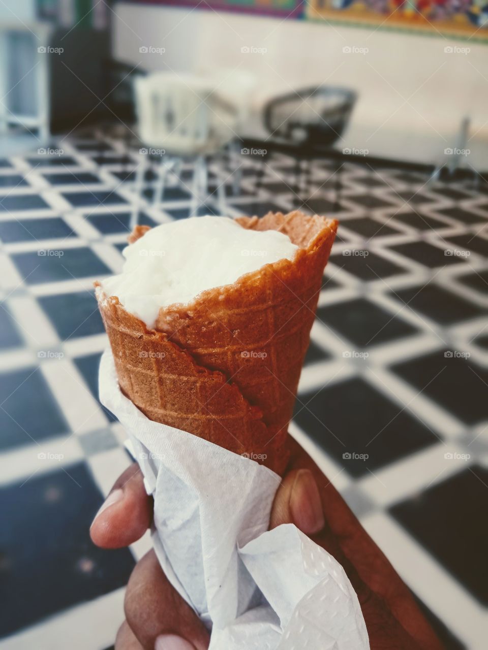 holding icecream cone against black and white tiles