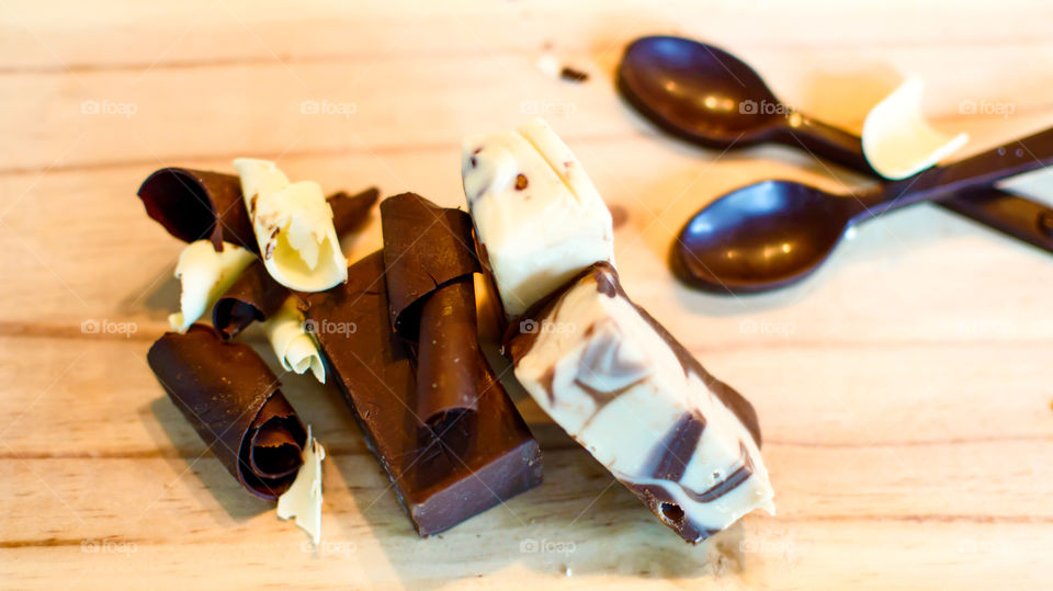 Chocolate background with spoons made of chocolate, marble fudge, dark chocolate block and white chocolate and dark chocolate shavings on wood high angle view 