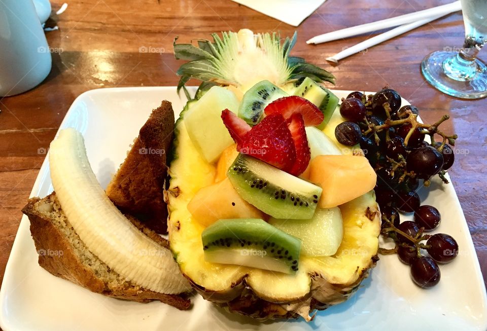 A fruit salad inside of a hollow pineapple and slices of banana bread 