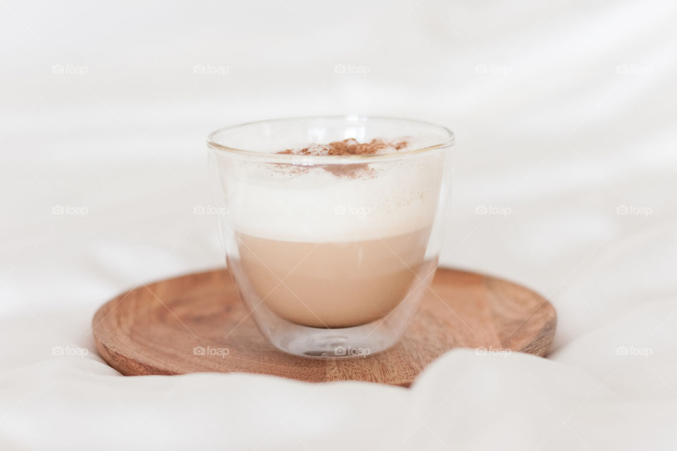 Cappuccino with cinnamon on a wooden plate on white bed linen