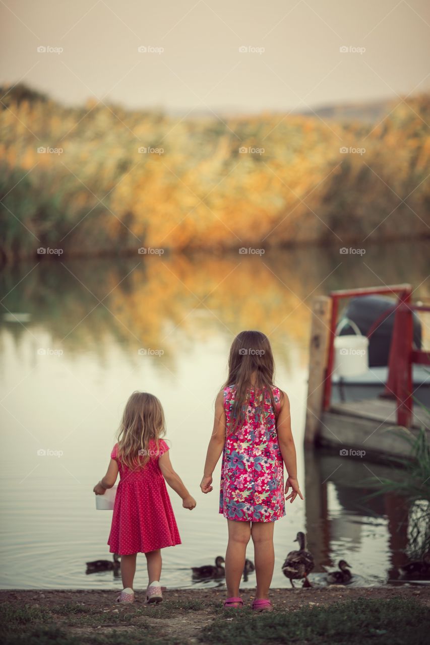 Little sisters near lake at sunset