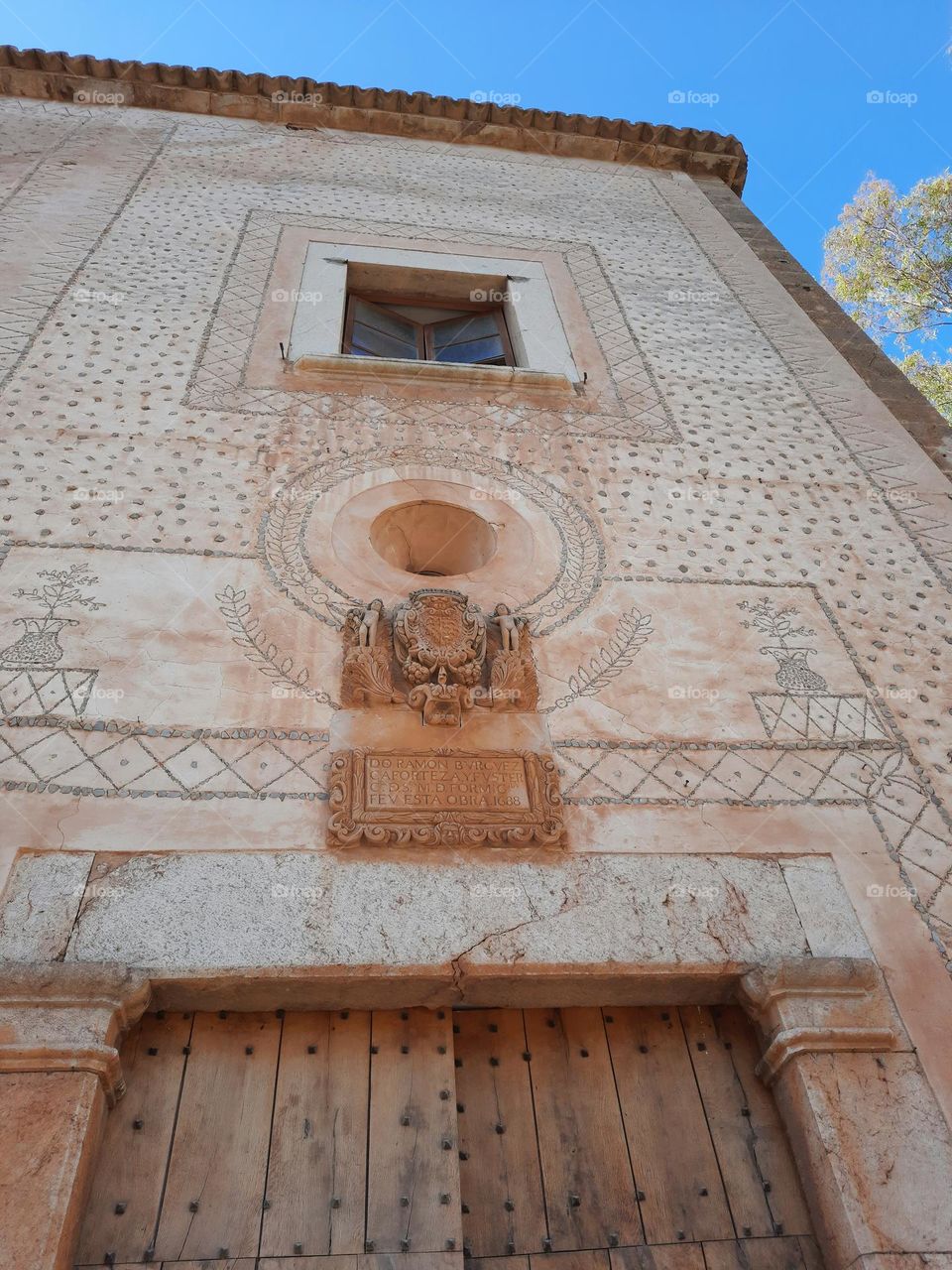 Mediterranean old manor facade. On the wall there is an ancient stone heraldic coat of arms, a window, a rounded window and a wood door. Majorca, Spain