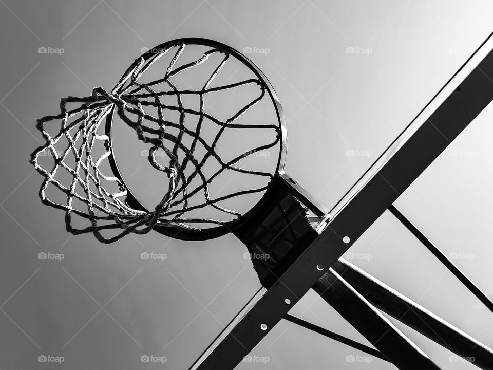 Looking up at a Basketball net on a beautiful sunny afternoon waiting for those slam dunks during game play , in black and white 