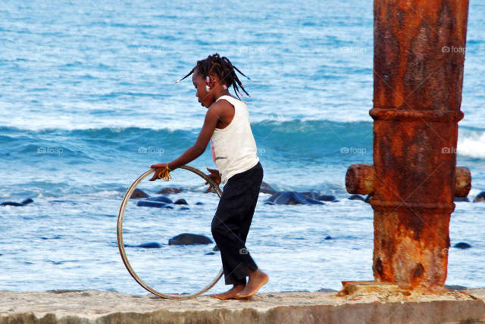 Young girl rolling a hoop on the beach, city of São Tomé, São Tomé & Principe